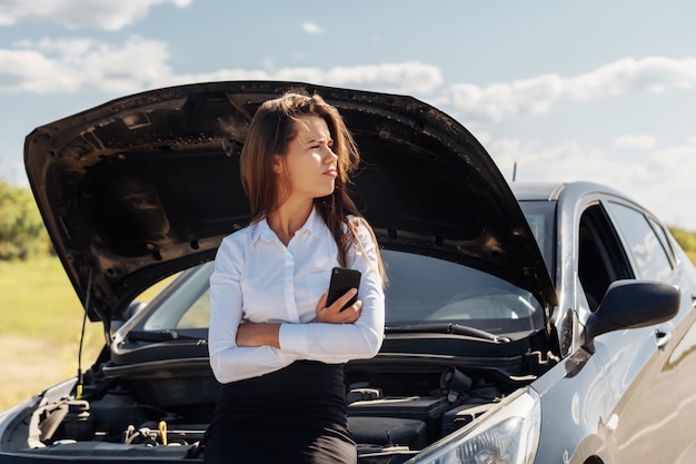 Belle femme d'affaires assis sur une voiture cassée