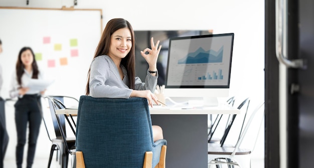 Une belle femme d'affaires assise sur son lieu de travail et faisant un signe de geste OK