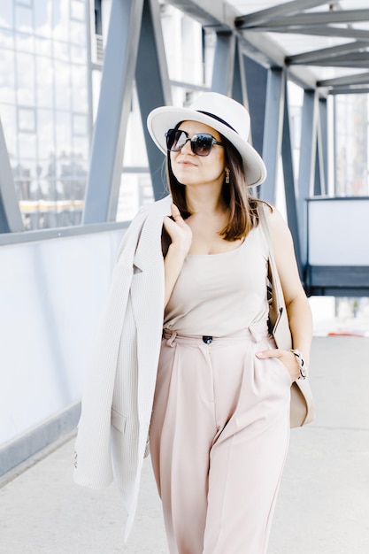 Belle femme d'affaires brune portant costume et chapeau blanc marchant dans la rue