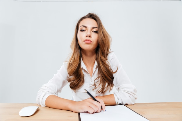 Belle femme d'affaires confiante assise à la table sur fond blanc