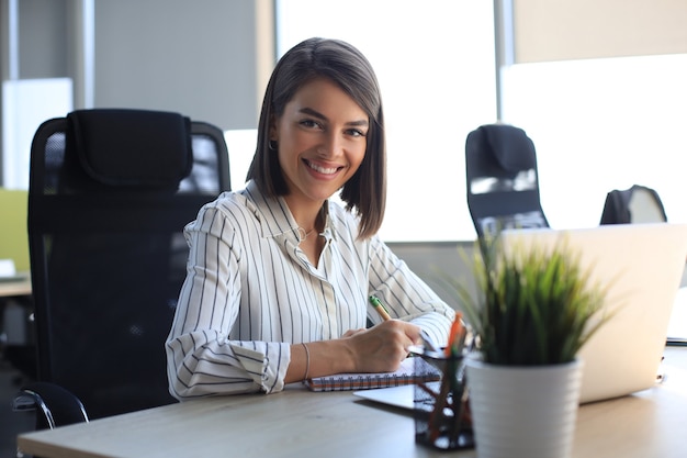 Une belle femme d'affaires écrit quelque chose alors qu'elle est assise au bureau.