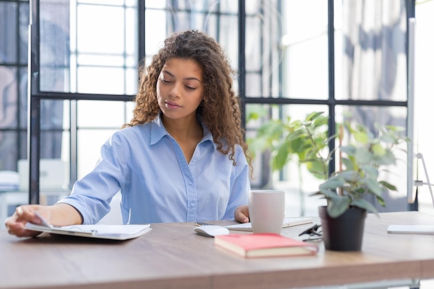 Une belle femme d'affaires examine des documents alors qu'elle est assise au bureau