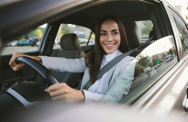 Belle femme d'affaires heureuse et prospère conduit une nouvelle voiture moderne de bonne humeur. Portrait de jolie femme pilote de voiture avec ceinture de sécurité