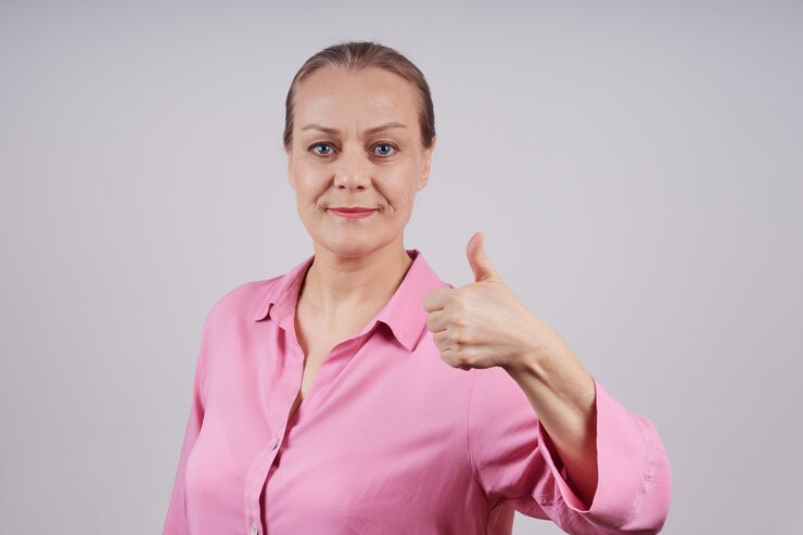 Belle femme d'affaires mature montrant le pouce vers le haut. Je suis satisfait du travail réussi. Photo sur fond gris avec espace copie.