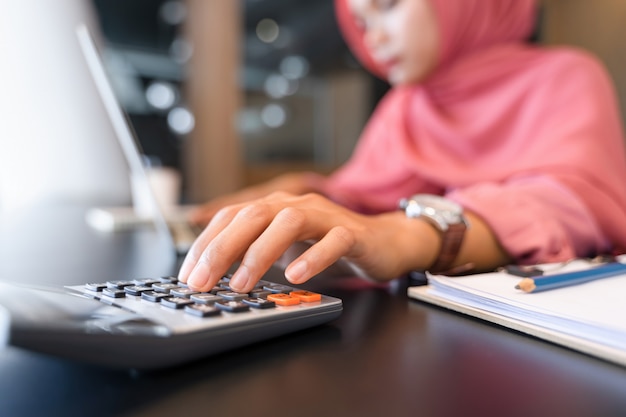 Belle femme d'affaires musulmane asiatique en hijab rose et vêtements décontractés travaillant avec calculatrice