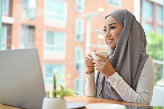 Belle femme d'affaires musulmane asiatique avec hijab se détend en sirotant un café le matin