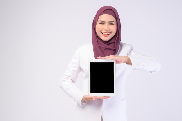 Belle femme d'affaires musulmane portant un costume blanc avec hijab tenant une tablette en studiox9