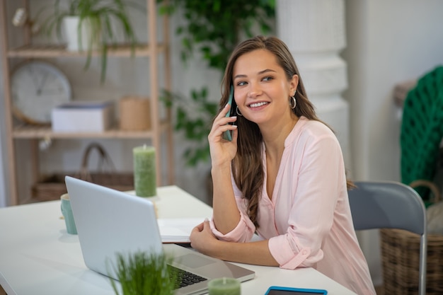 Belle femme d'affaires occupée assis devant l'ordinateur portable tout en ayant une conversation téléphonique