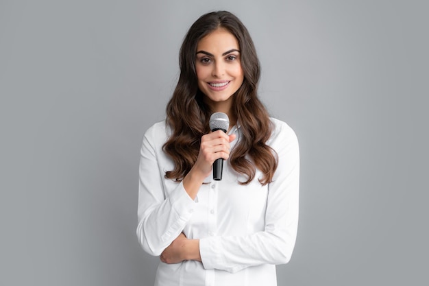 Belle femme d'affaires parle à la conférence Fille élégante chantant des chansons avec microphone tenant un micro au karaoké posant sur fond gris