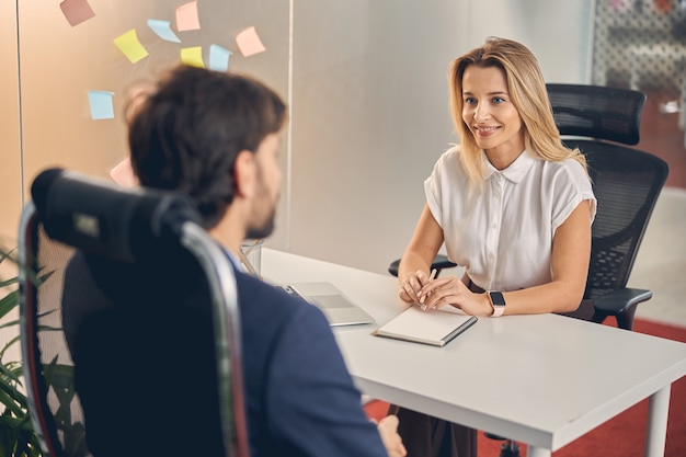 Belle femme d'affaires regardant l'homme et souriant tout en étant assis à la table avec un ordinateur portable