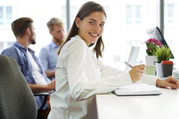 Belle femme d'affaires regarde la caméra et sourit tout en travaillant au bureau.