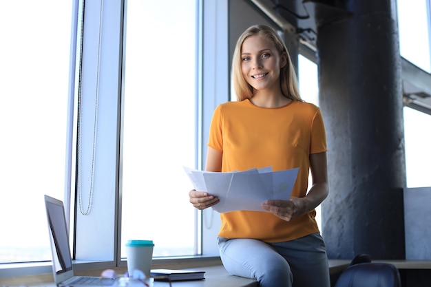 Belle femme d'affaires souriante est assise au bureau et regarde la caméra.