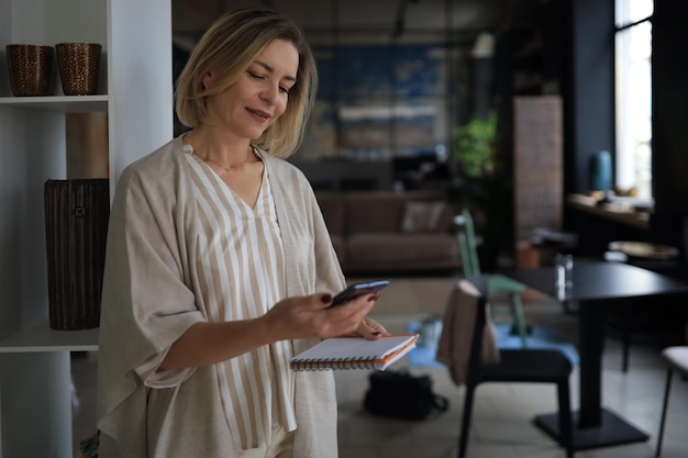 Belle femme d'affaires utilise son smartphone avec le sourire tout en se tenant au bureau.