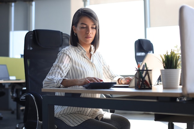 Belle femme d'affaires en vêtements décontractés intelligents travaillant sur ordinateur portable au bureau.