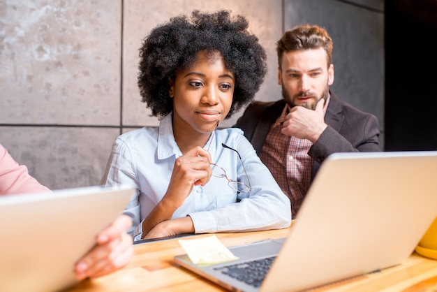 Belle femme africaine avec un bel homme caucasien travaillant avec un ordinateur portable à l'intérieur du bureau moderne