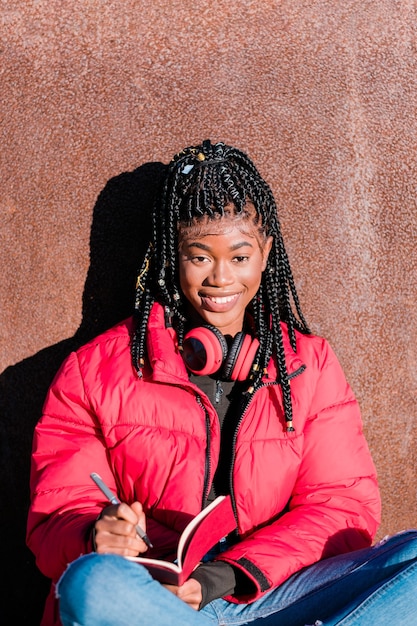 Belle femme africaine avec des écouteurs à l'extérieur Femme noire écrivant dans un cahier