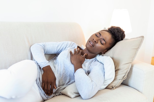 Belle femme africaine malade de ressentir une douleur dans la poitrine en position couchée sur le canapé.