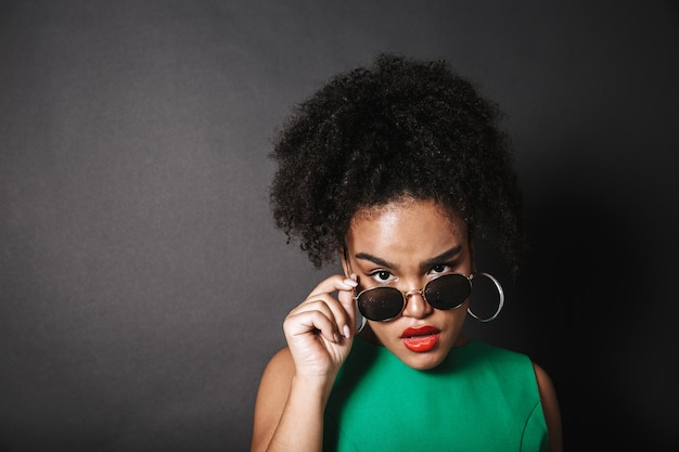 Belle femme africaine portant des lunettes de soleil posant isolé sur un espace noir