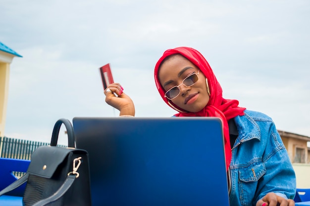 Belle femme africaine se sentant enthousiasmée par ce qu'elle a vu sur son ordinateur portable alors qu'elle tient sa carte de crédit.