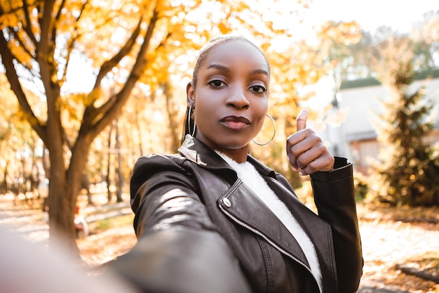 Une belle femme africaine souriante tient un téléphone à la main discutant avec des amis vidéochat montrant le pouce vers le haut comme