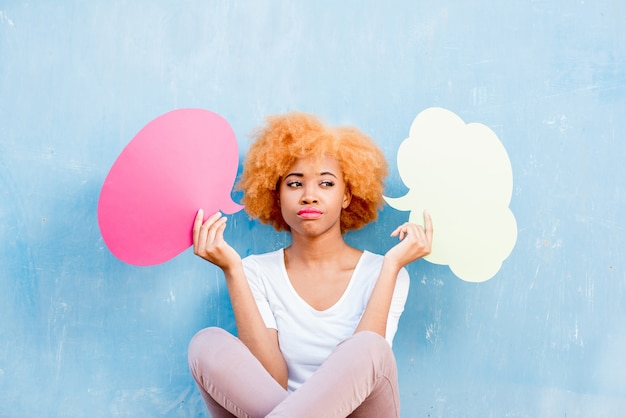 Belle femme africaine tenant des bulles réfléchies colorées sur le fond bleu du mur