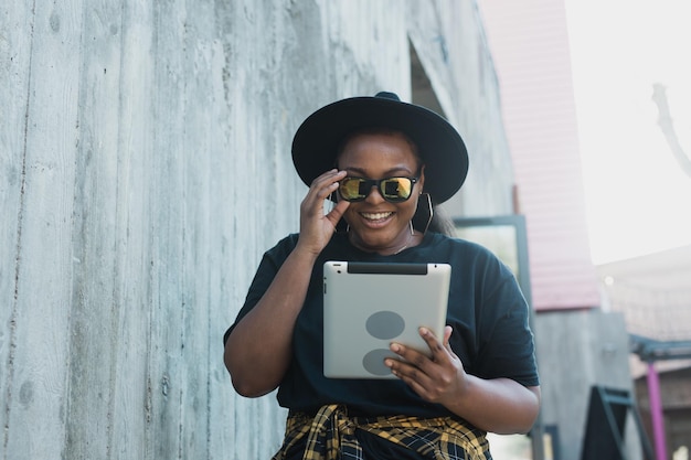 Belle femme afro-américaine à l'aide d'une tablette numérique en regardant un film à l'extérieur ou en parlant d'appel vidéo ou de réseaux sociaux Réussi blogueur influenceur streaming vidéo et communication en ligne