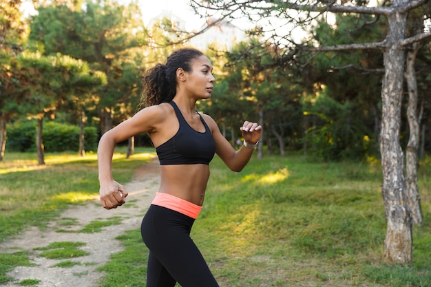 Belle femme afro-américaine des années 20 portant des vêtements de sport noirs, traversant le parc verdoyant