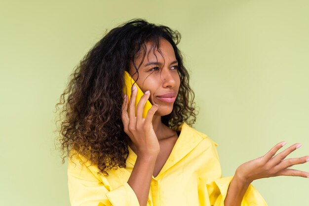 Photo belle femme afro-américaine en chemise décontractée sur fond vert parler sur téléphone mobile choqué confus