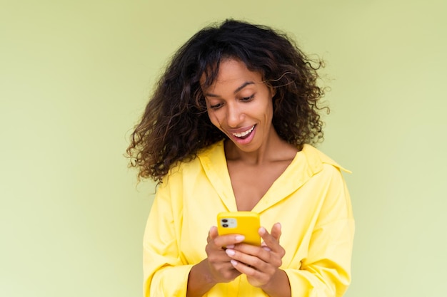 Belle femme afro-américaine en chemise décontractée sur fond vert tient un téléphone portable avec un sourire