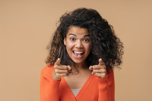 Belle femme afro-américaine heureuse pointant du doigt la caméra isolée sur fond