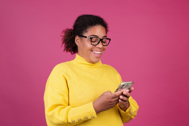 Belle femme afro-américaine sur un mur rose en tapant un message sur un téléphone portable excité heureux