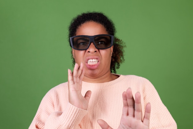 Belle femme afro-américaine sur un mur vert avec des lunettes de cinéma 3d regardant l'émotion de dégoût de film