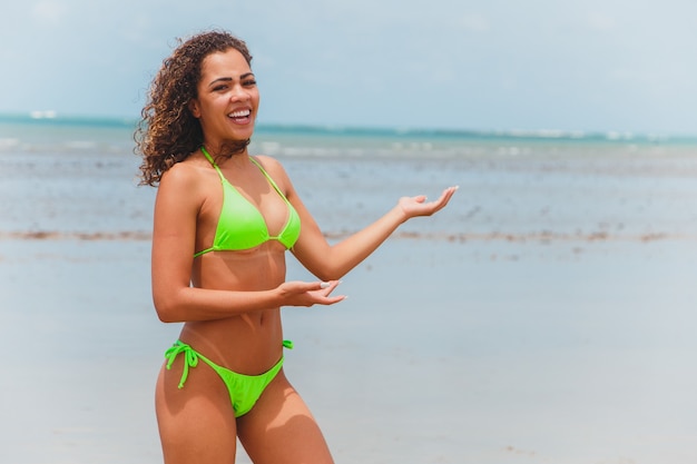 Belle femme afro-brésilienne sur une plage à rio grande do norte, sourit, sentant la liberté et les vagues de la mer, profitant de ses vacances d'été avec un soleil et une chaleur merveilleux