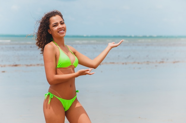 Belle femme afro-brésilienne sur une plage à rio grande do norte, sourit, sentant la liberté et les vagues de la mer, profitant de ses vacances d'été avec un soleil et une chaleur merveilleux