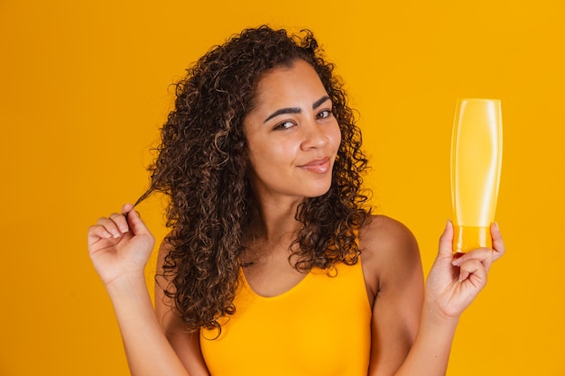 Belle femme afro tenant une bouteille de gel shampooing dans ses mains