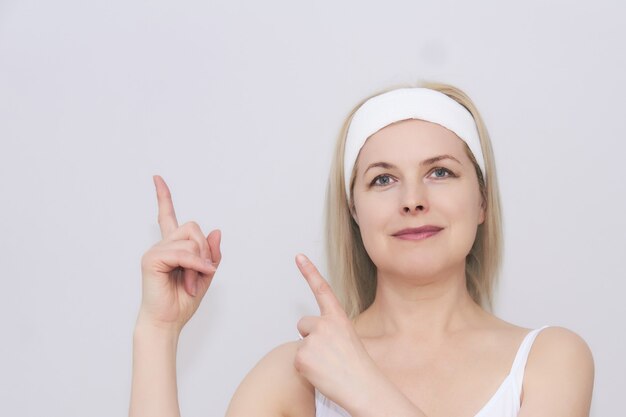 Belle femme d'âge moyen dans un bandeau pour les soins de beauté montre l'espace à côté d'elle