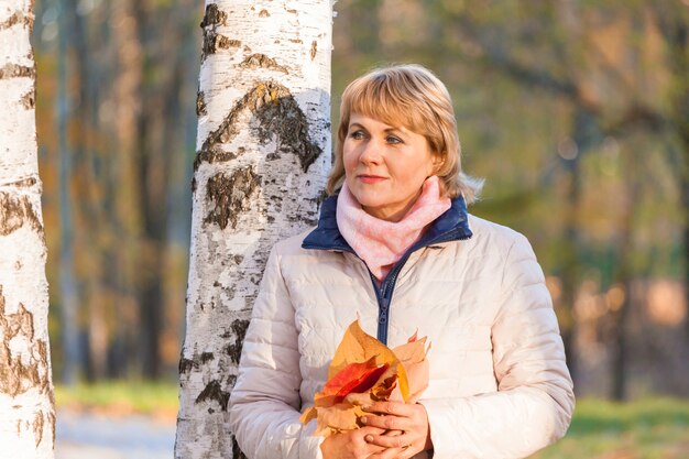 Belle femme d'âge moyen sur la nature à l'automne. Une femme mûre se promène dans le parc, elle est heureuse.