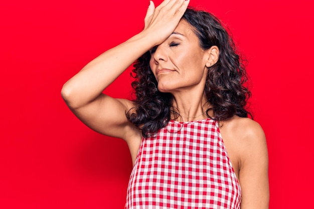 Belle femme d'âge moyen portant un t-shirt décontracté sans manches surprise avec la main sur la tête pour erreur, rappelez-vous l'erreur. oublié, mauvaise notion de mémoire.