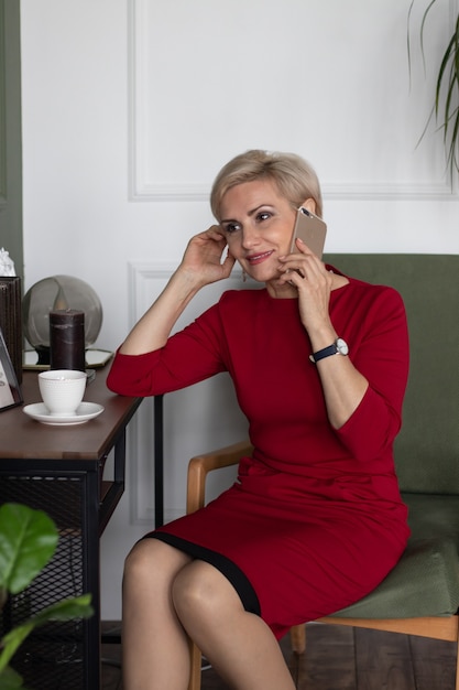 belle femme d'âge moyen en robe rouge assise sur une chaise avec téléphone portable