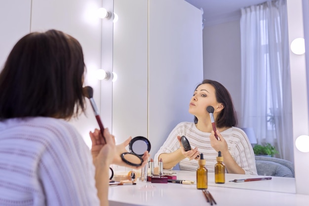 Belle femme d'âge moyen se maquillant devant un miroir