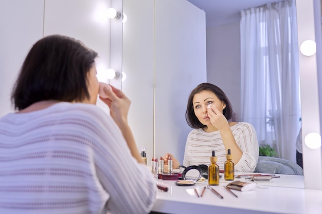 Belle femme d'âge moyen se maquillant devant un miroir