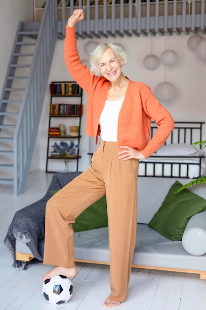 Photo belle femme âgée dans un appartement confortable regardant un match de football belle femme aux cheveux gris avec un ballon de football concept de vieillesse active