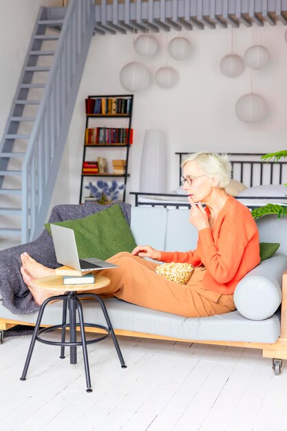 Photo belle femme âgée dans un appartement confortable travaille sur un ordinateur portable belle femme aux cheveux gris travaille en ligne ou regarde des films étudie et communique le concept de vieillesse active