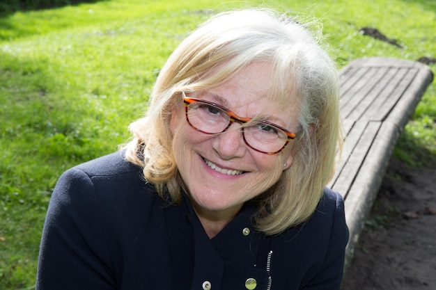 Belle femme âgée avec des lunettes sur un banc en bois