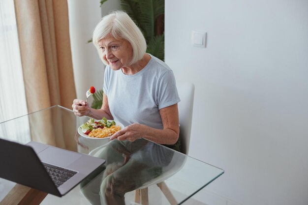 Belle femme âgée mangeant de la nourriture à la maison à l'intérieur