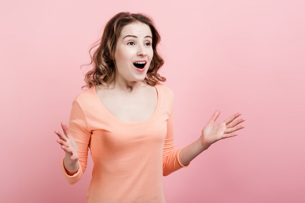 Une belle femme agréablement surprise ouvrit les bras contre un mur rose