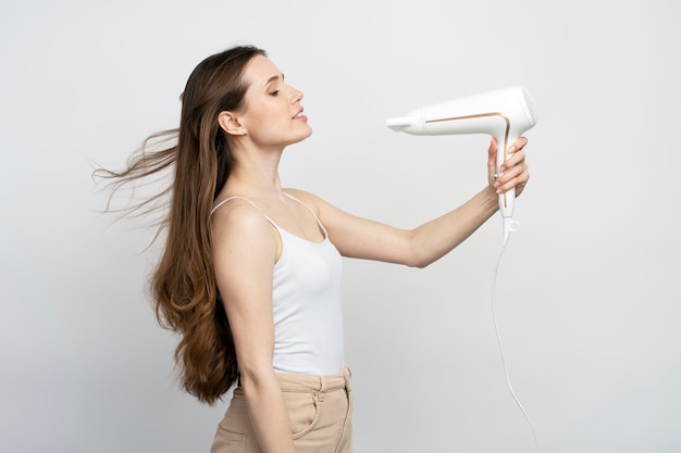 Belle femme à l'aide d'un sèche-cheveux isolé sur fond blanc Routine matinale de soins capillaires de beauté