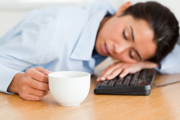 Belle femme allongée sur un clavier tout en tenant une tasse de café