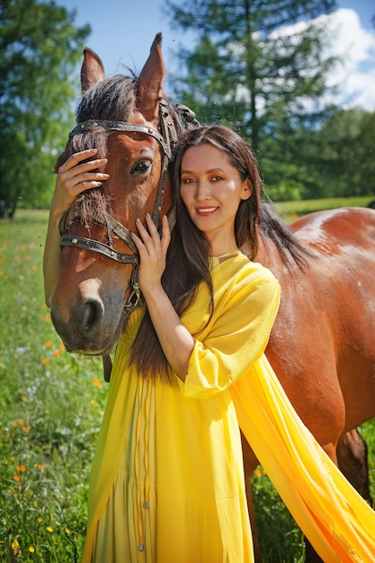 Une belle femme d'apparence asiatique vêtue d'une robe jaune se promène avec un cheval en été dans l'Altaï.