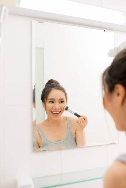 Belle femme appliquant un fard à joues dans sa salle de bain